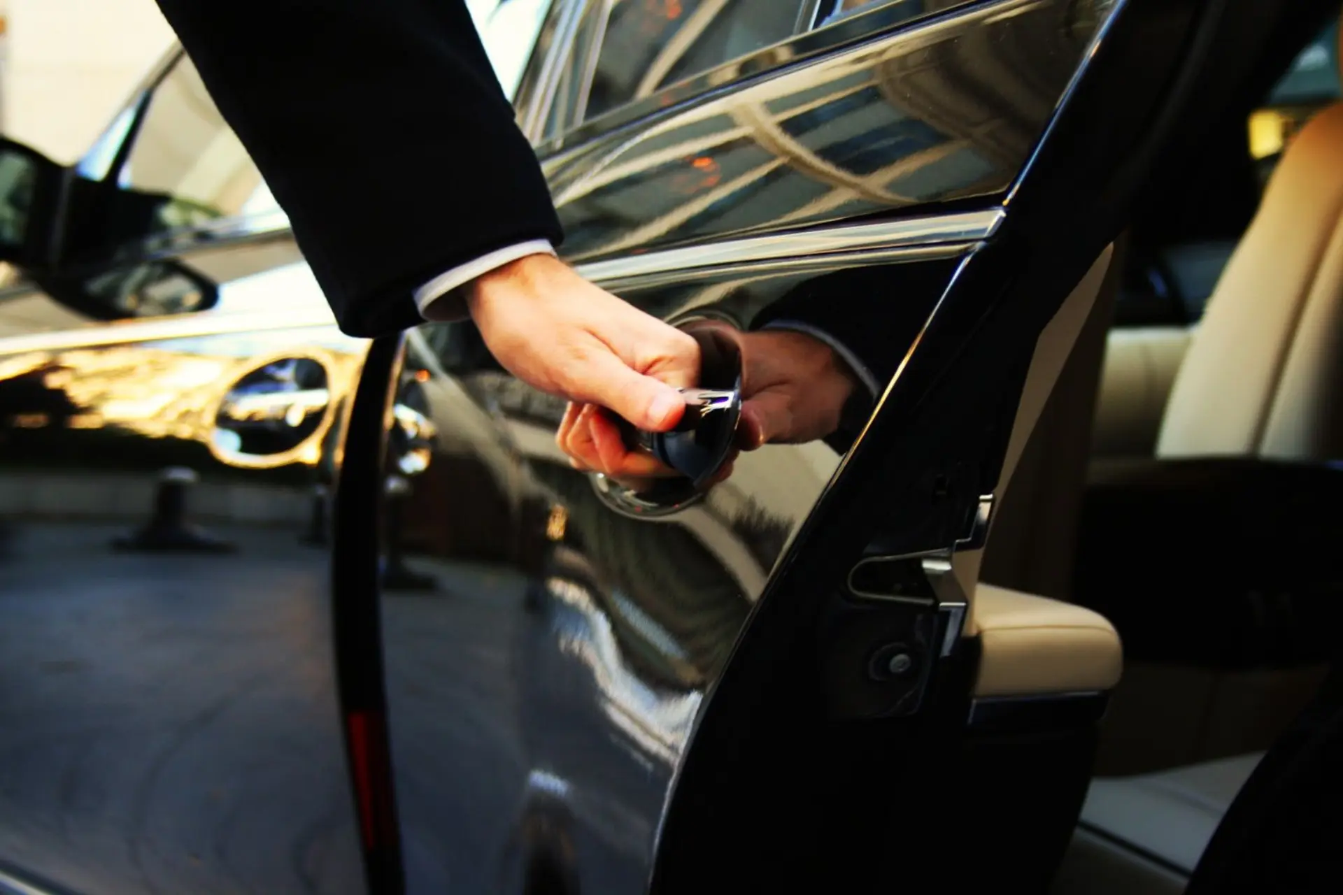A professional chauffeur opening the rear door of a black luxury SUV at a terminal curb — Harmony Limo flight-tracked MIA, FLL, PBI and Ocean Reef Club airport transfers with Harmony Limo